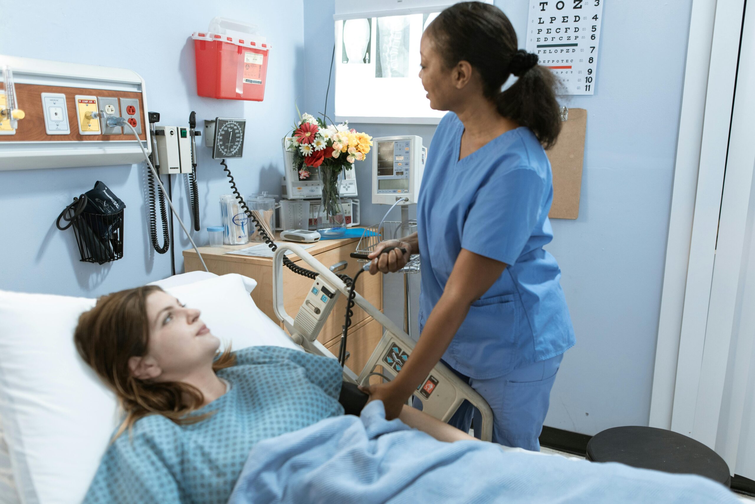 Home Nurse providing care to a patient in a hospital room with medical equipment.